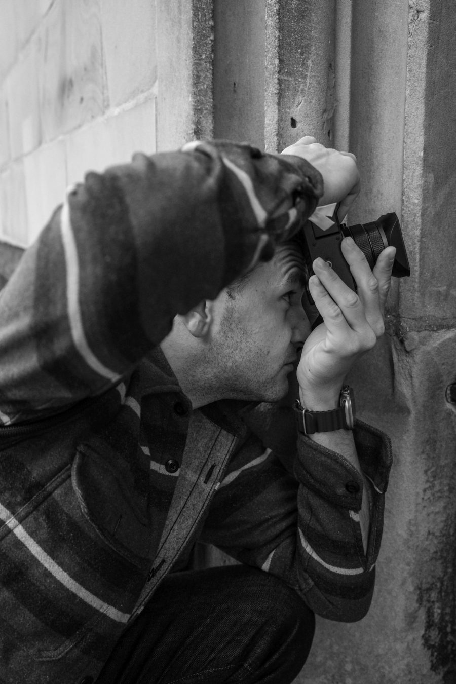 Philipp Bevier crouching by a stone wall, taking a photo with a compact camera